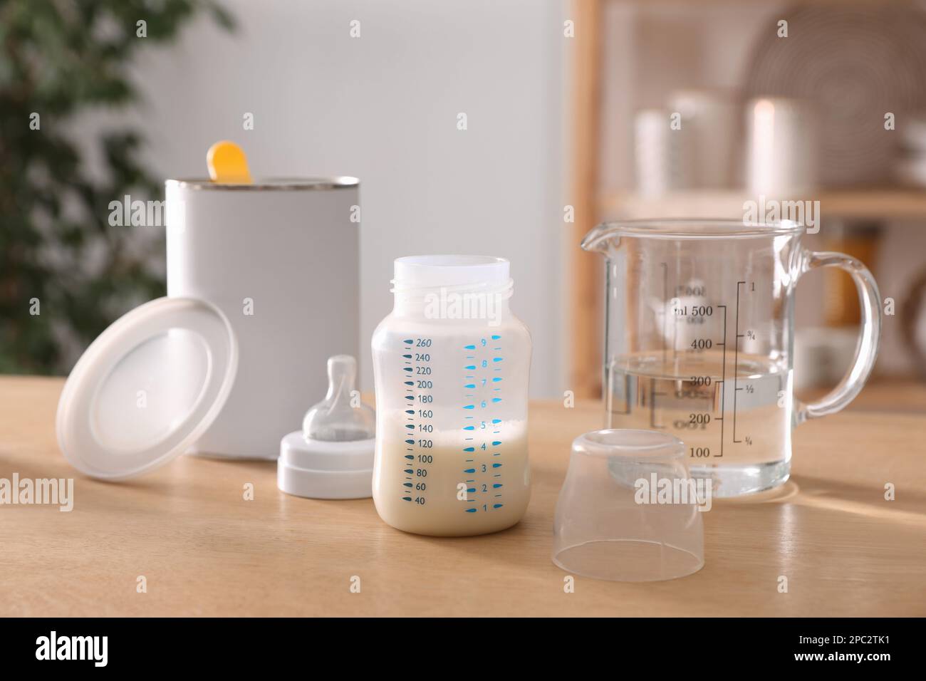 Feeding bottle with infant formula, can and jug of water on wooden table indoors. Baby milk Stock Photo