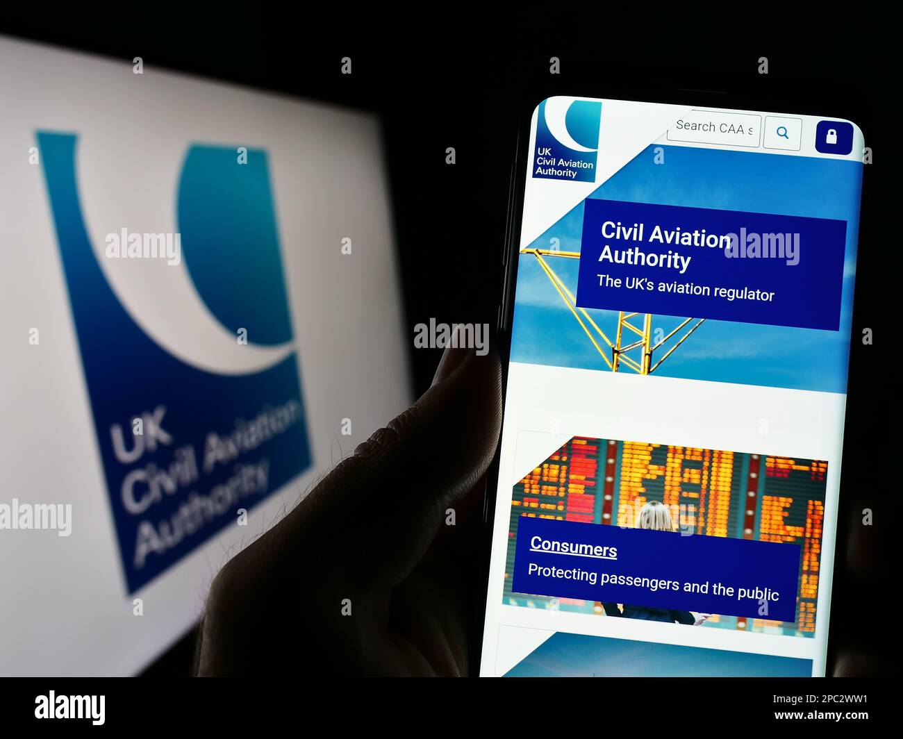 Person holding cellphone with website of British regulator Civil Aviation Authority (CAA) on screen with logo. Focus on center of phone display. Stock Photo