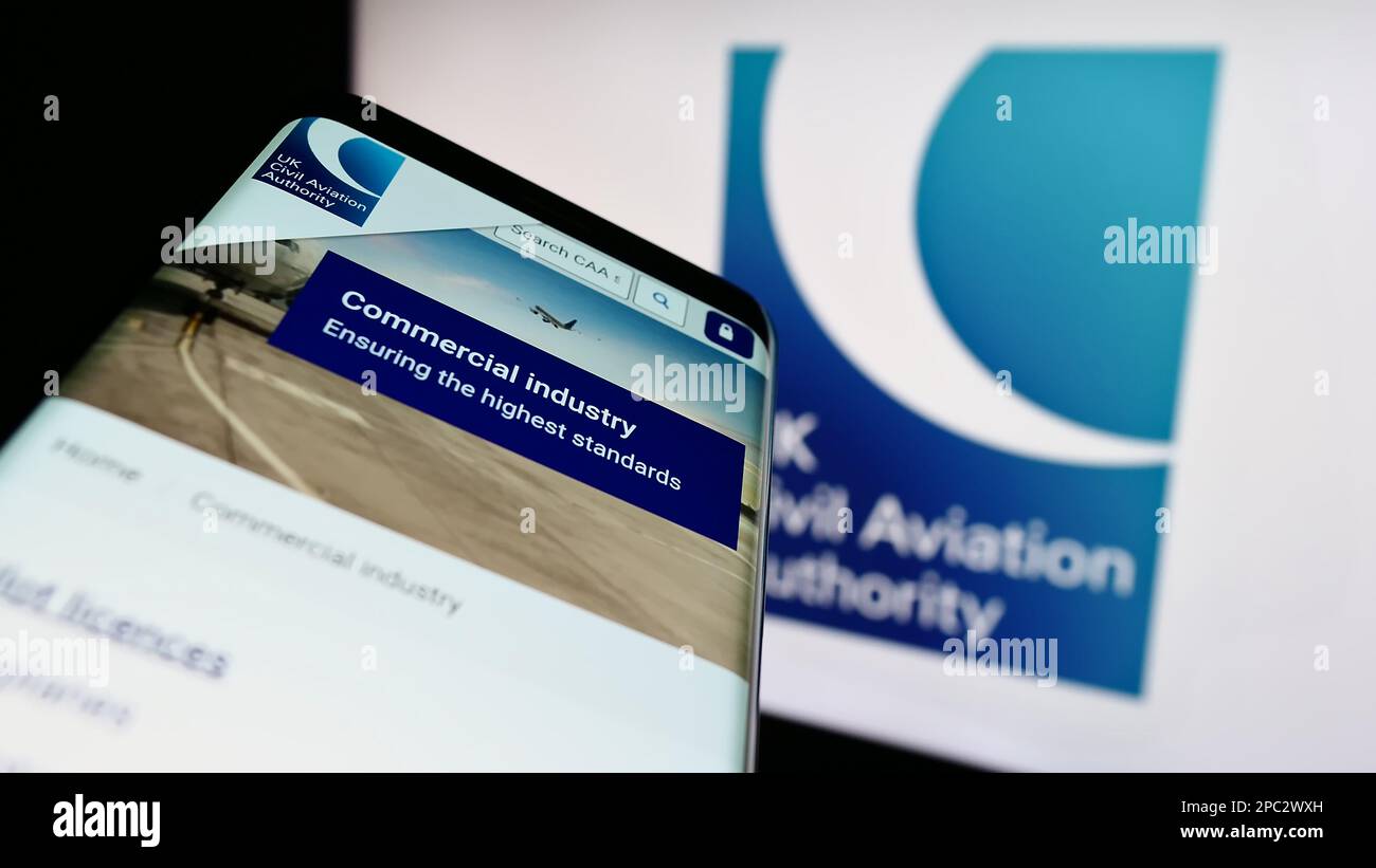 Smartphone with webpage of British regulator Civil Aviation Authority (CAA) on screen in front of logo. Focus on top-left of phone display. Stock Photo