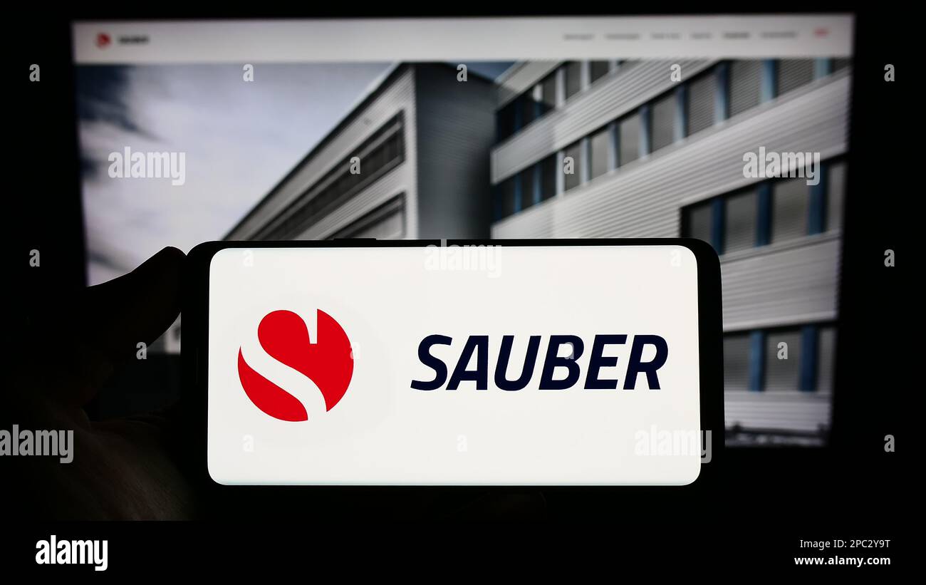 Person holding smartphone with logo of Swiss automotive company Sauber Motorsport AG on screen in front of website. Focus on phone display. Stock Photo