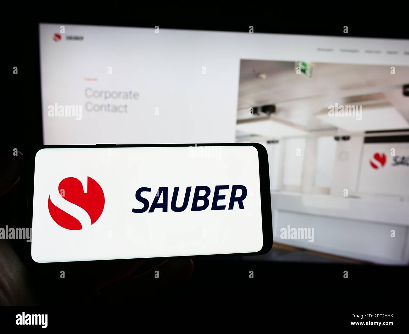 Person holding cellphone with logo of Swiss automotive company Sauber Motorsport AG on screen in front of webpage. Focus on phone display. Stock Photo
