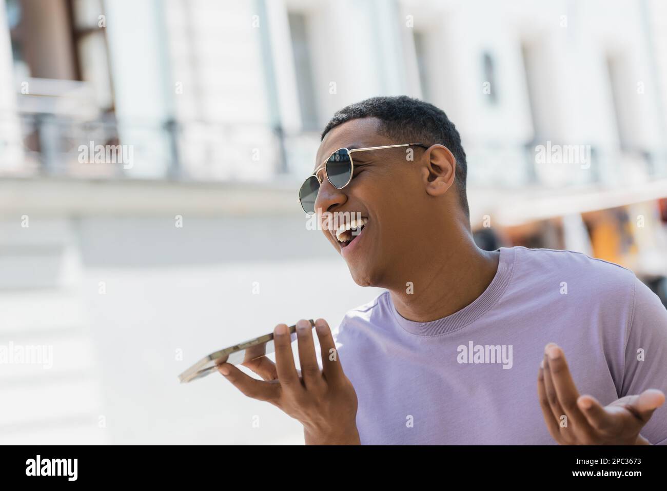 Positive african american man in sunglasses recording voice message on urban street in summer,stock image Stock Photo