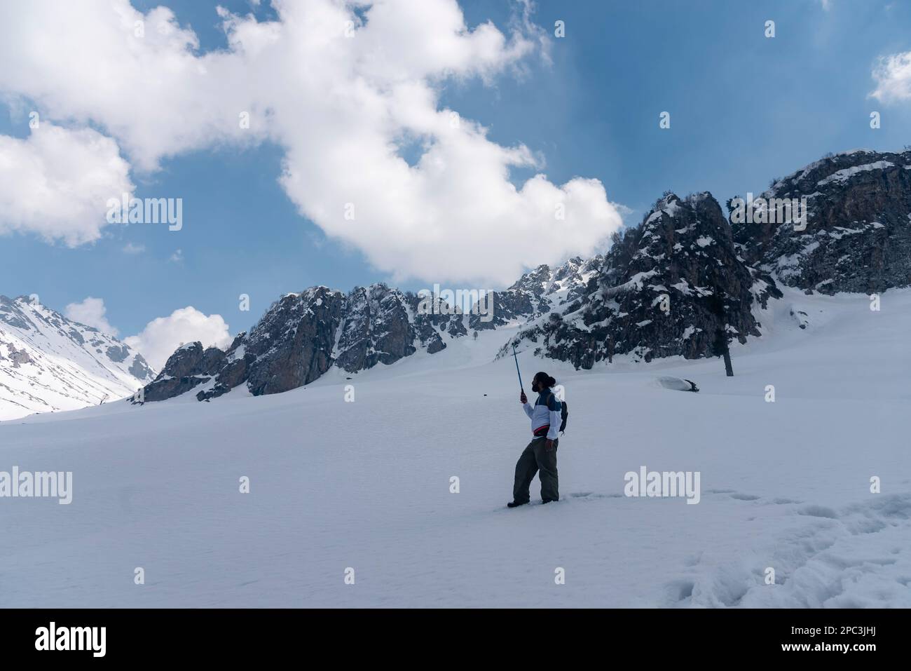 A trekker enroute his way through a snow covered mountain during a sunny day at Lidwas at an elevation of 3220 m in mountains of Himalayas. The Zabarwan Range is a short sub-mountain range between Pir Panjal and Great Himalayan Range in the central part of the Kashmir Valley. The highest peak of Zabarwan Mountain Range is Mahadev Peak at 13,013 feet (3,966 m). The Zabarwan Range has crystalline rocks such as granite, schists and phyllites with embedded lime stone, which form the core of its parent range. Moreover Zabarwan Mountain Range possesses great Himalayan Mountain Range with rich wildli Stock Photo