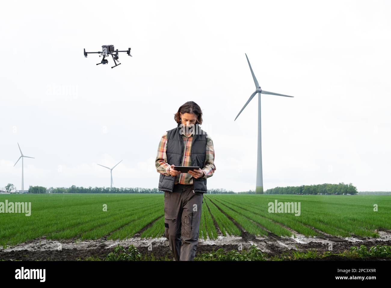 Farmer with drone on a field with wind turbines on a horizon. Smart