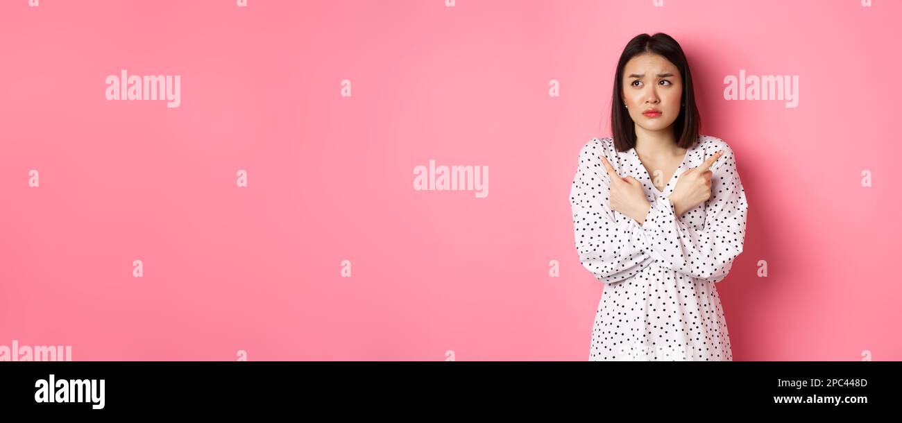 Hesitant Concerned asian woman having doubts, pointing sideways and looking left ...