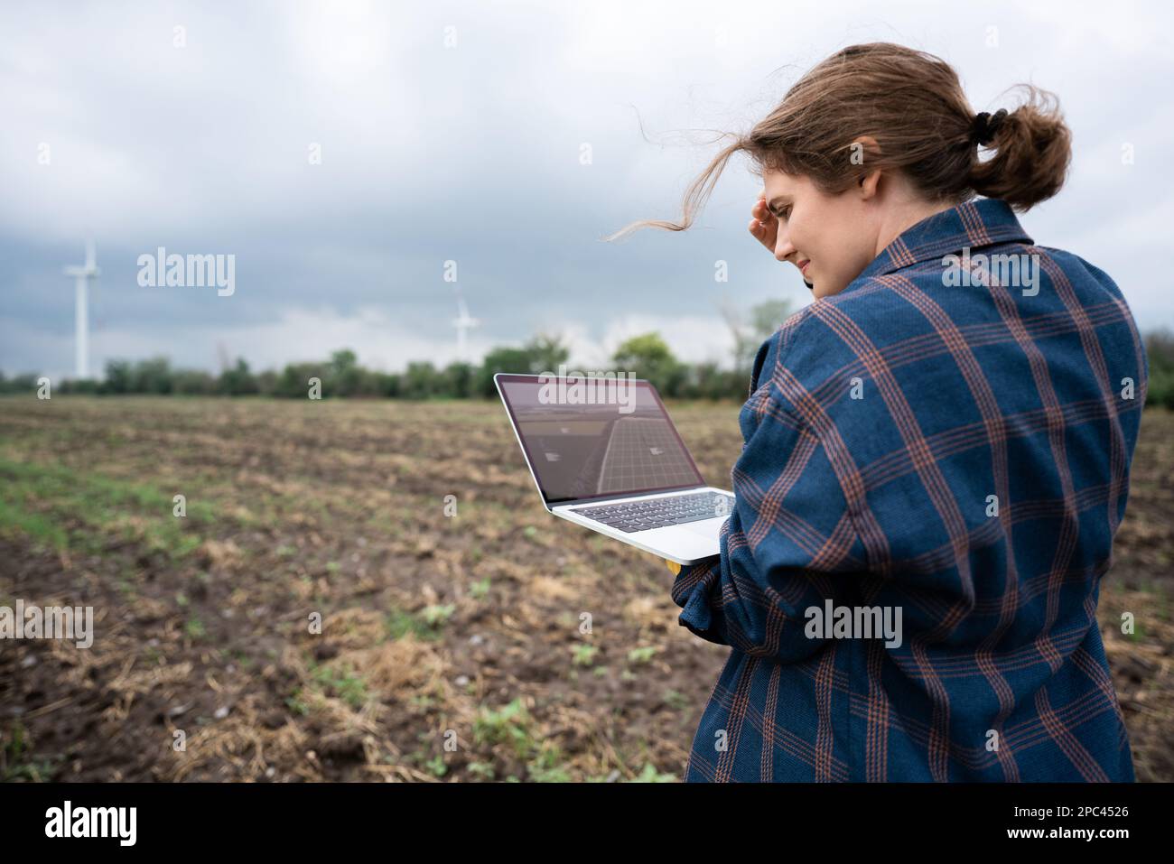 Farmer with laptop on the field. Wind turbines on a horizon. Smart sustainable farming and agriculture digitalization Stock Photo