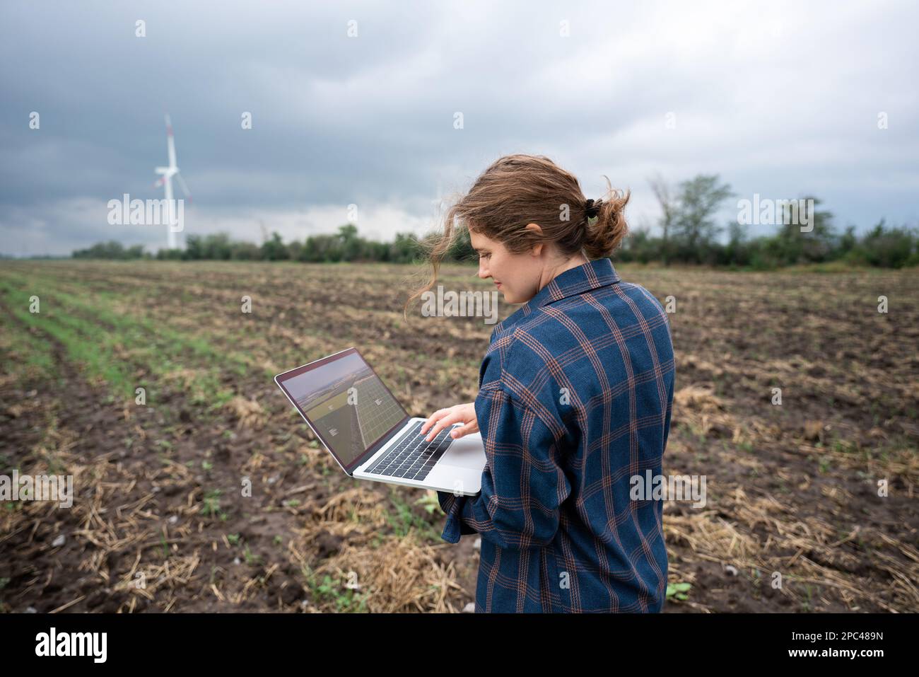 Farmer with laptop on the field. Wind turbines on a horizon. Smart sustainable farming and agriculture digitalization Stock Photo