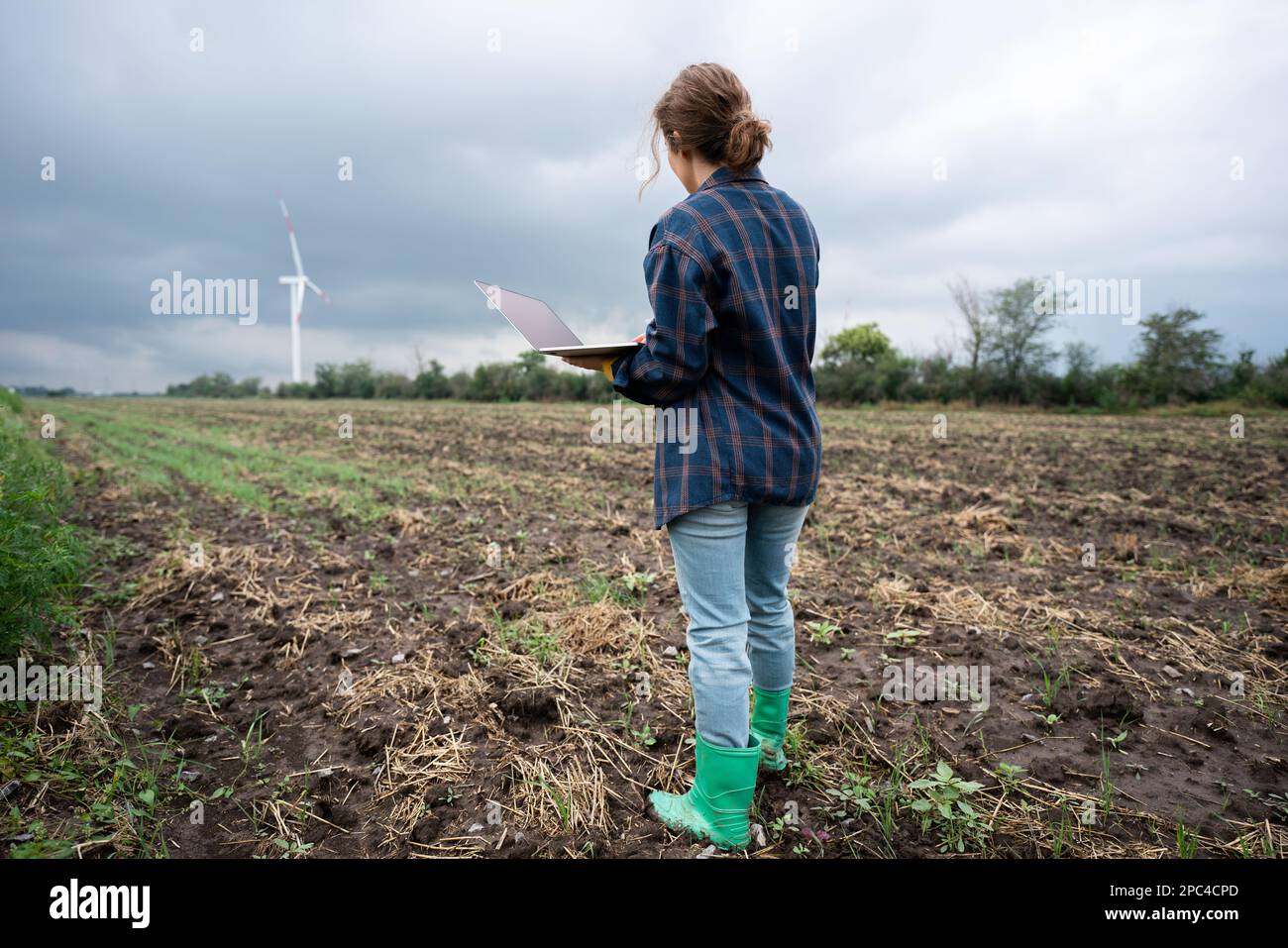 Farmer with laptop on the field. Wind turbines on a horizon. Smart sustainable farming and agriculture digitalization Stock Photo
