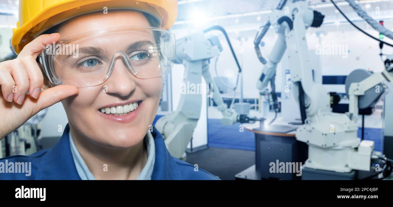 Portrait of woman engineer in helmet and eyeglasses on a background of robots at smart factory Stock Photo