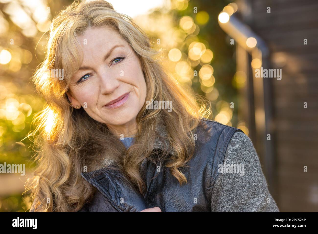 Attractive thoughtful middle aged woman outside smiling in golden hour sunlight Stock Photo