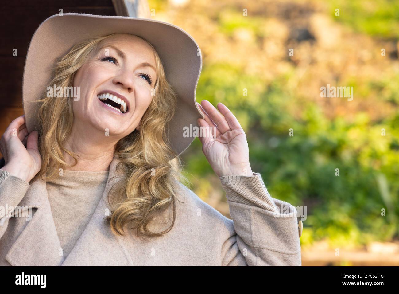 Attractive happy smiling stylish middle aged woman with perfect teeth outside wearing a hat Stock Photo