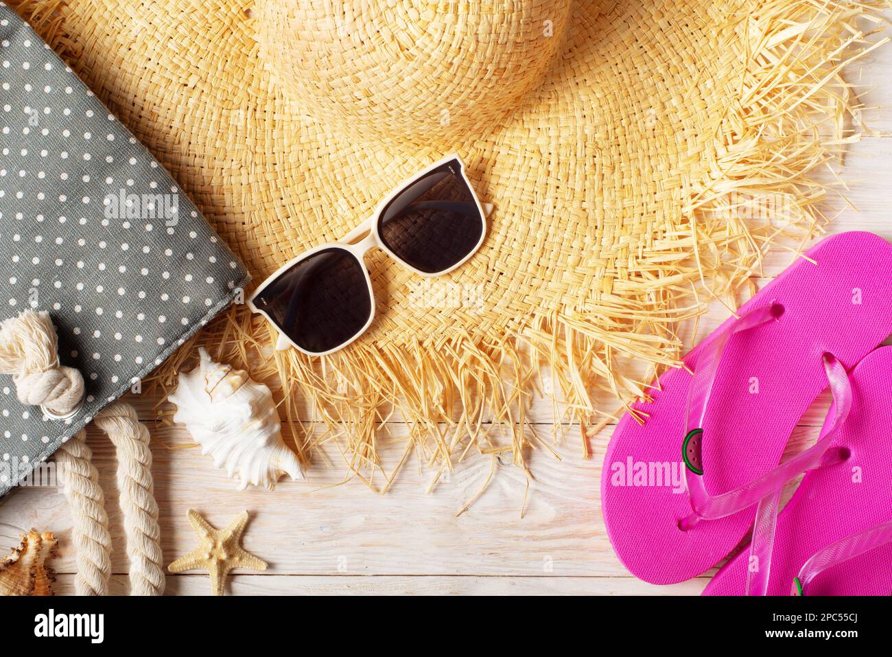 Straw hat sunglasses flip flops and beach bag on white wooden ...