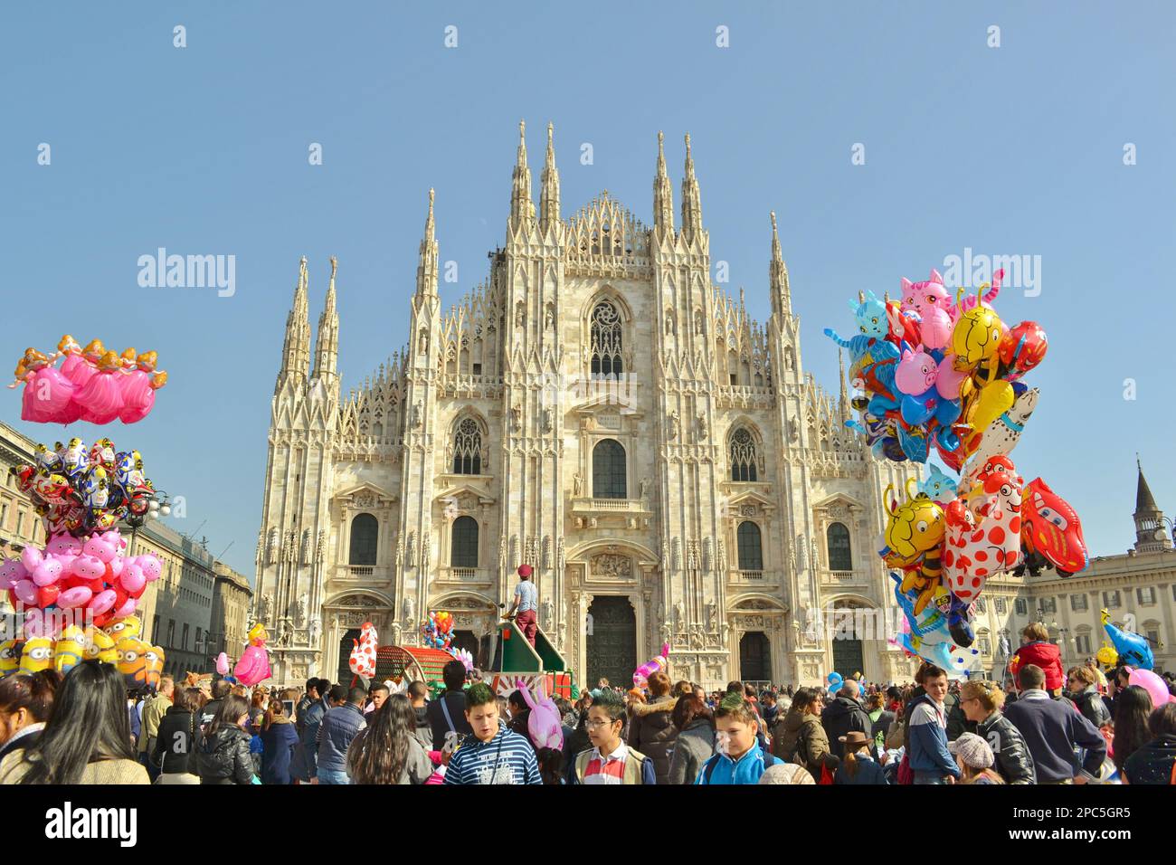 People celebrating Carnival in Duomo square of Milan in front of the famous medieval cathedral. Happy men and women and colorful balloons. Stock Photo