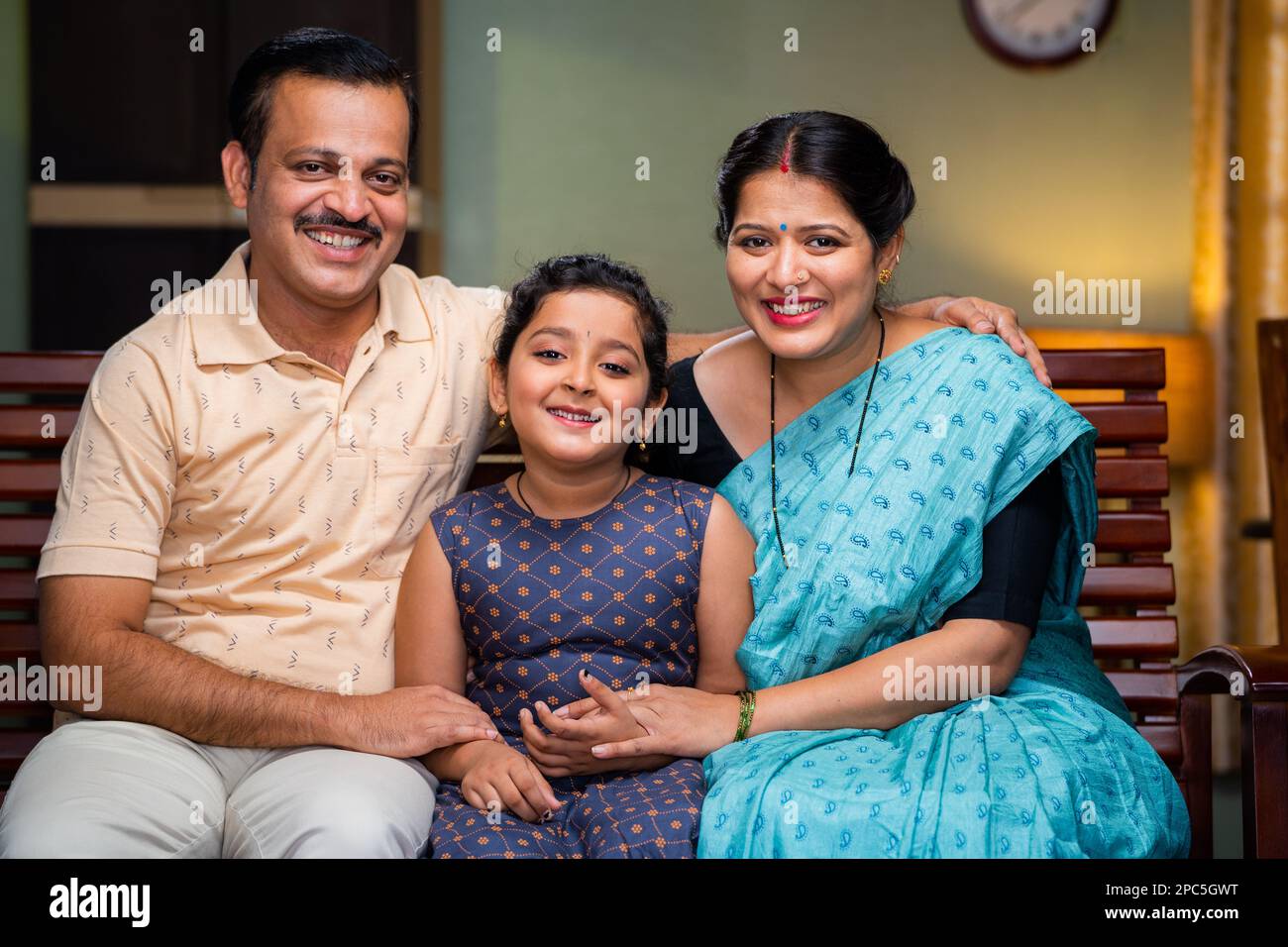 Happy smiling couple with daughter looking camera while sitting on sofa at home - concept of relationship, family photo posing and togetherness Stock Photo