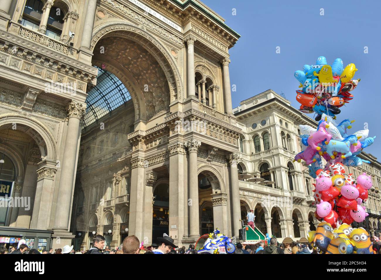People celebrating Carnival in Duomo square of Milan in front of Vittorio Emanuele II Gallery fashion mall. Hapèpy crowd and colorful balloons. Stock Photo