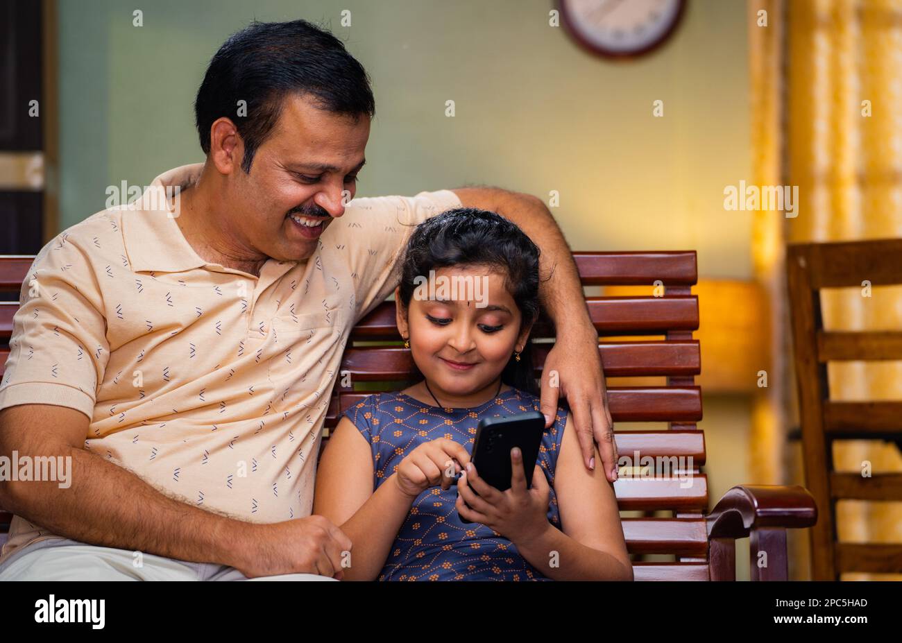 Young teenager kid teaching from mobile phone to father while sitting on sofa at home - concept of technology, intelligence and family bonding Stock Photo