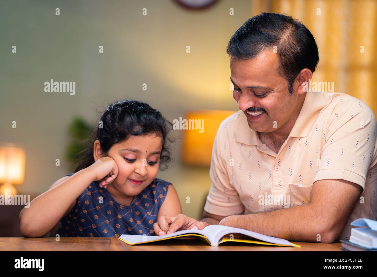 focus on father, Father helping his daughter for reading book at home during evening - concept of education, caring family and responsibility Stock Photo