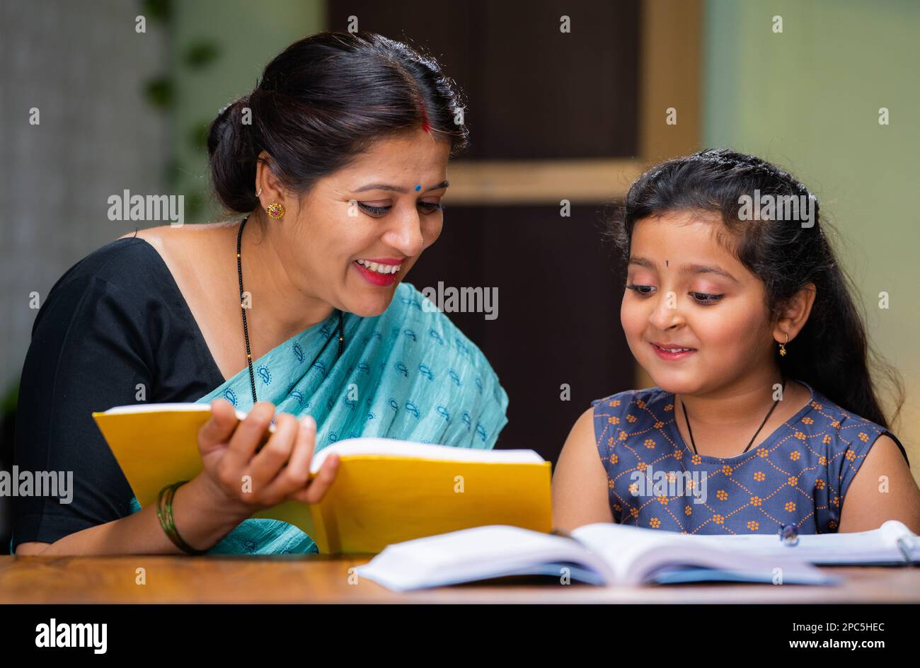 Mother teaching his daughter for reading book at home - concept of education, home tutor and parenthood Stock Photo