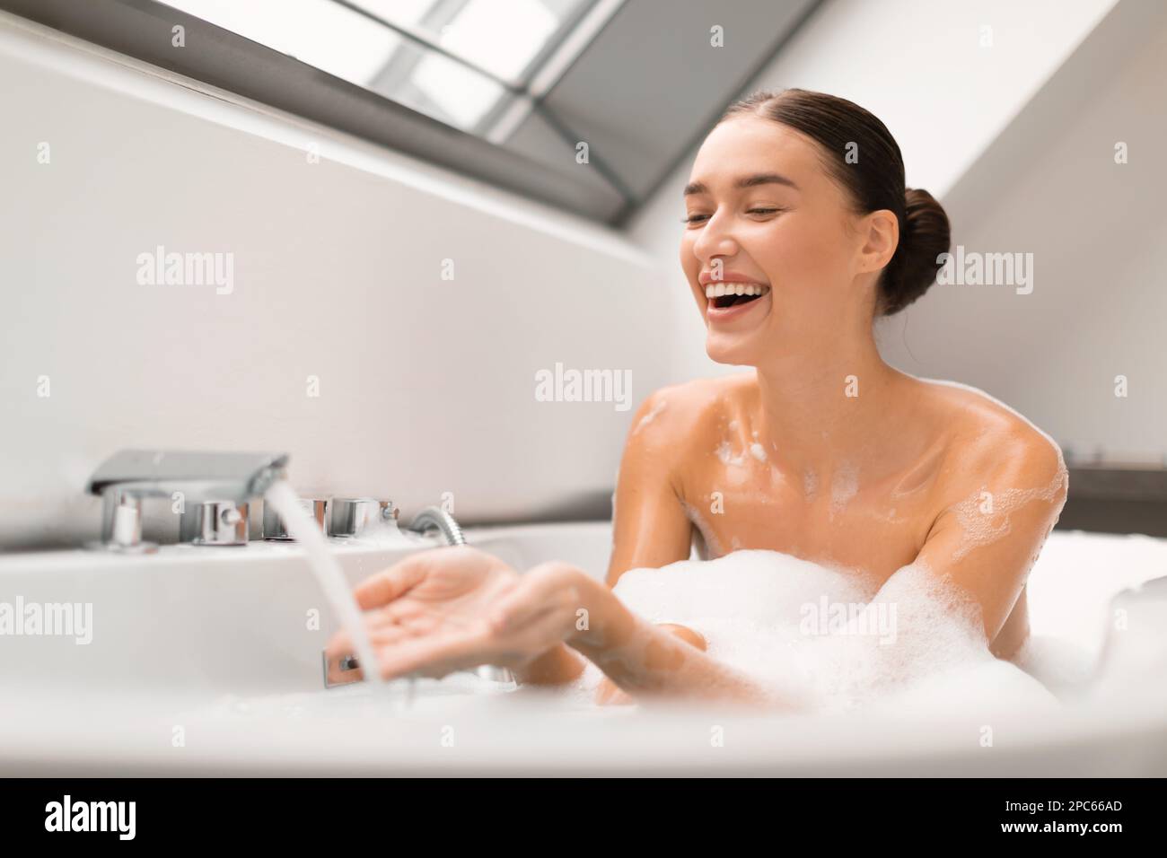 Woman Taking Bath Touching Running Water From Tap In Bathroom Stock
