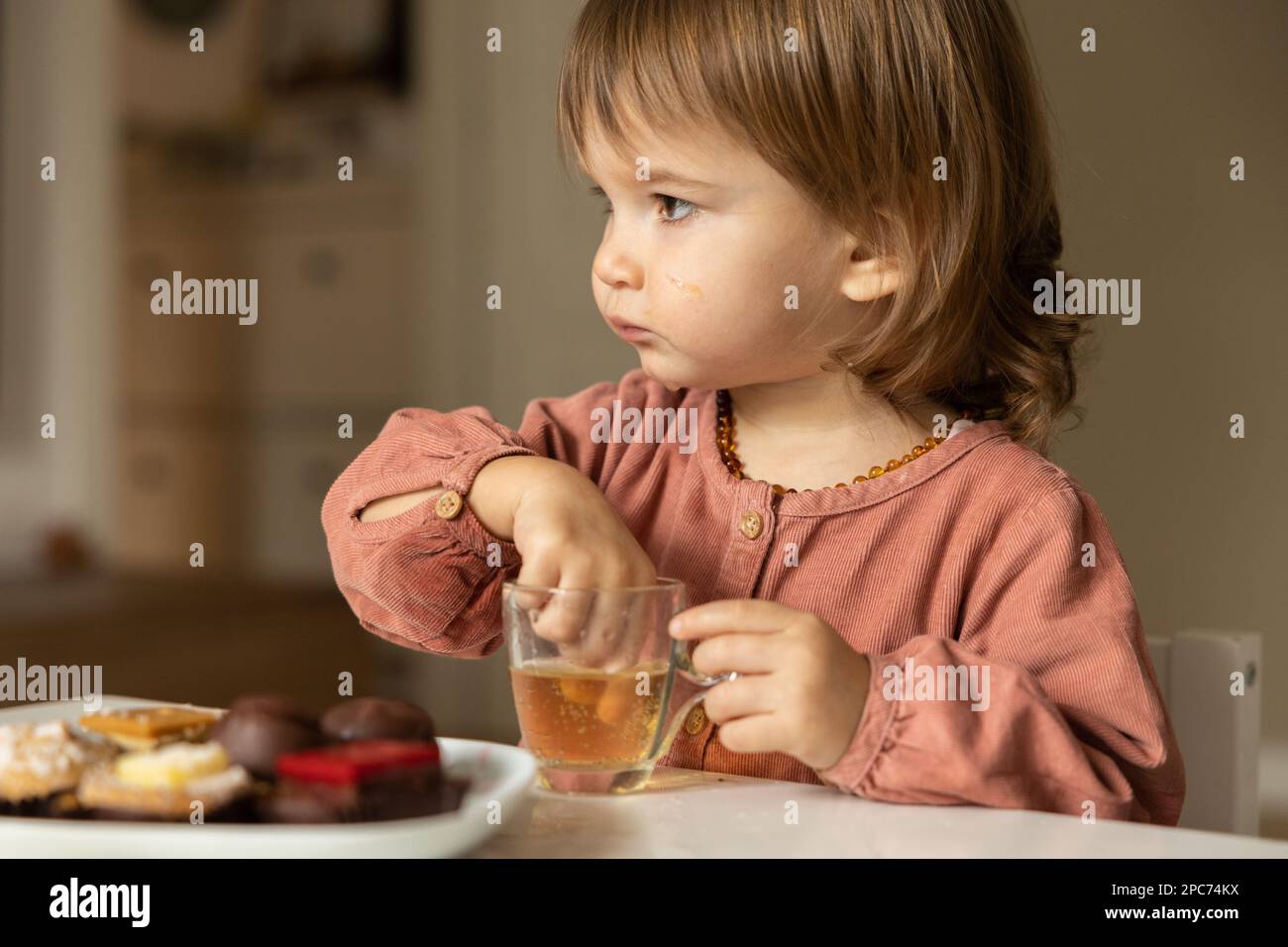 Little girl eats at the table and sticks her fingers into a glass of