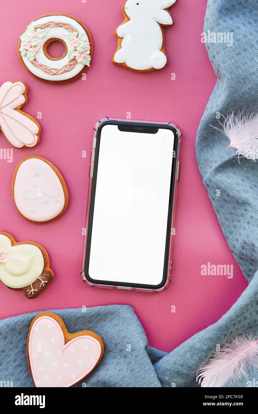Mockup of screen phone among Easter seasonal aesthetics pastry cookies on pink background flat lay. Happy Easter. Stock Photo