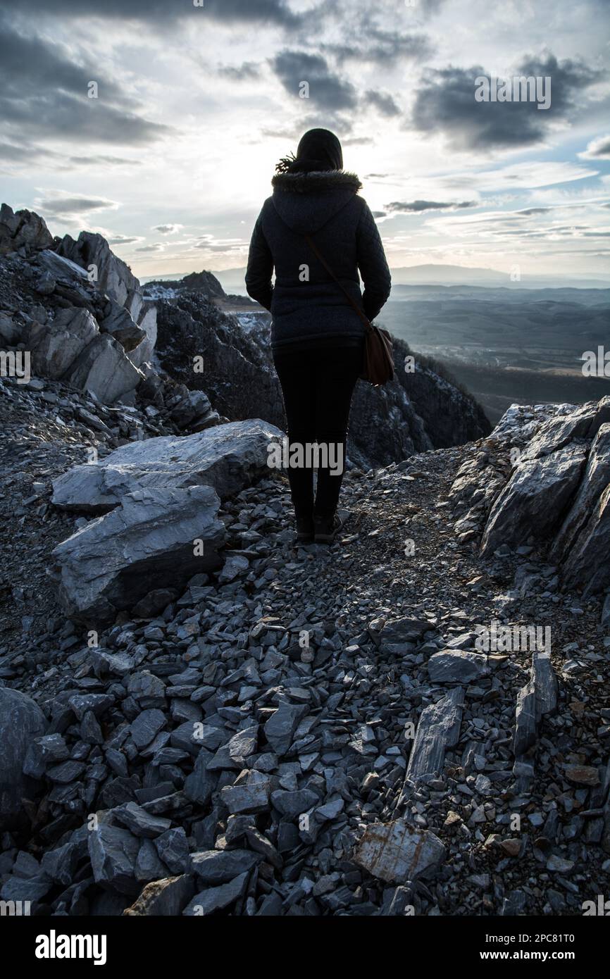 A woman stands with her back on the edge of the cliff. Rocky mountain ...