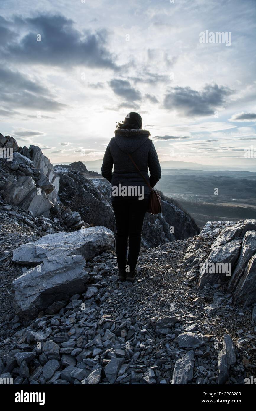 A woman stands with her back on the edge of the cliff. Rocky mountain ...
