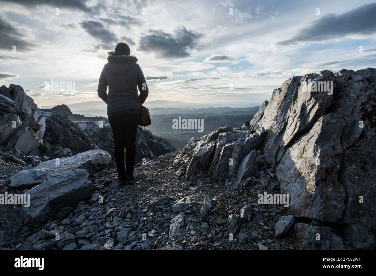 A woman stands with her back on the edge of the cliff. Rocky mountain ...