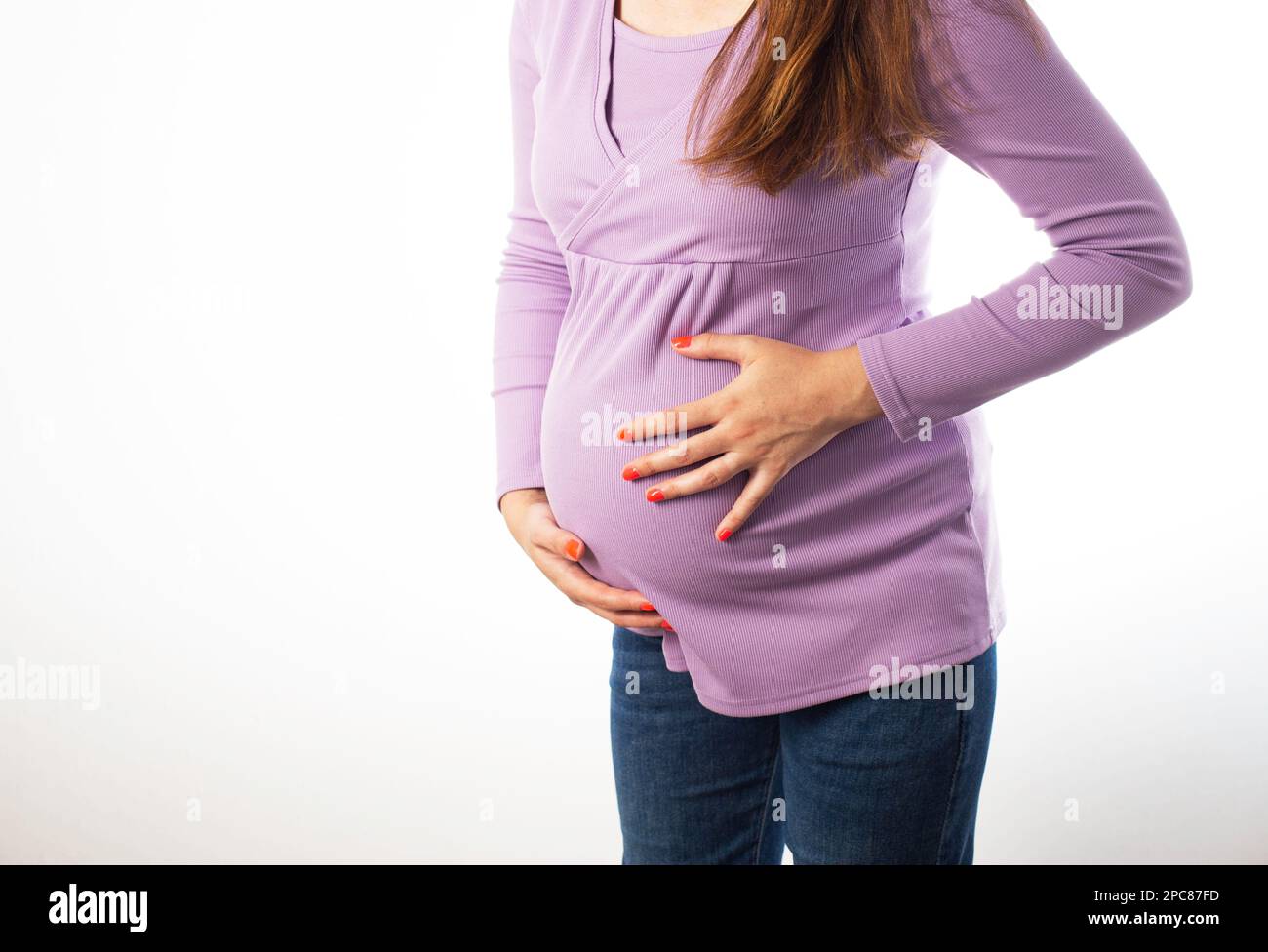 Pregnant girl holding on to her swollen belly on a white background