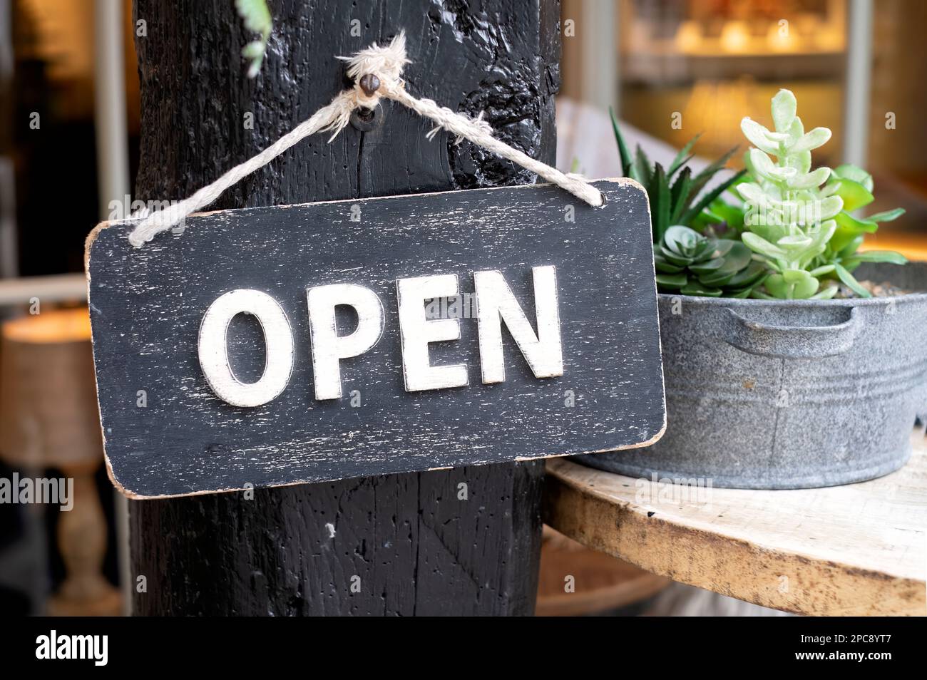 A small wooden rustic We are Open sign outside a premises. The sign is photographed close up and is hanging on a wooden support outside the shop Stock Photo