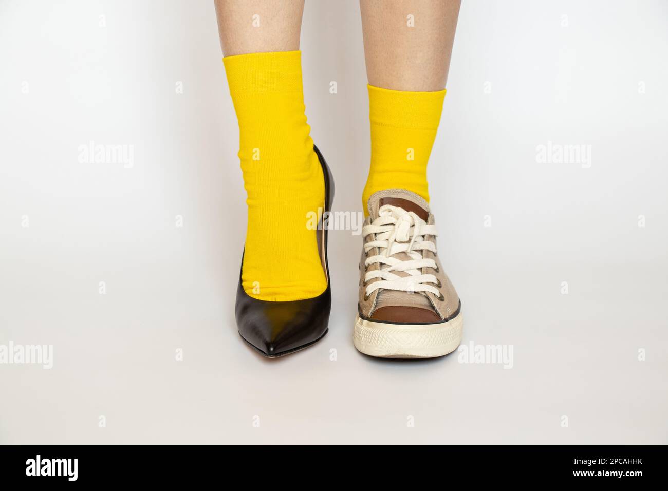 Different shoes on the girl's legs, high heeled shoes and sports sneakers in yellow socks on a white background, fashion Stock Photo