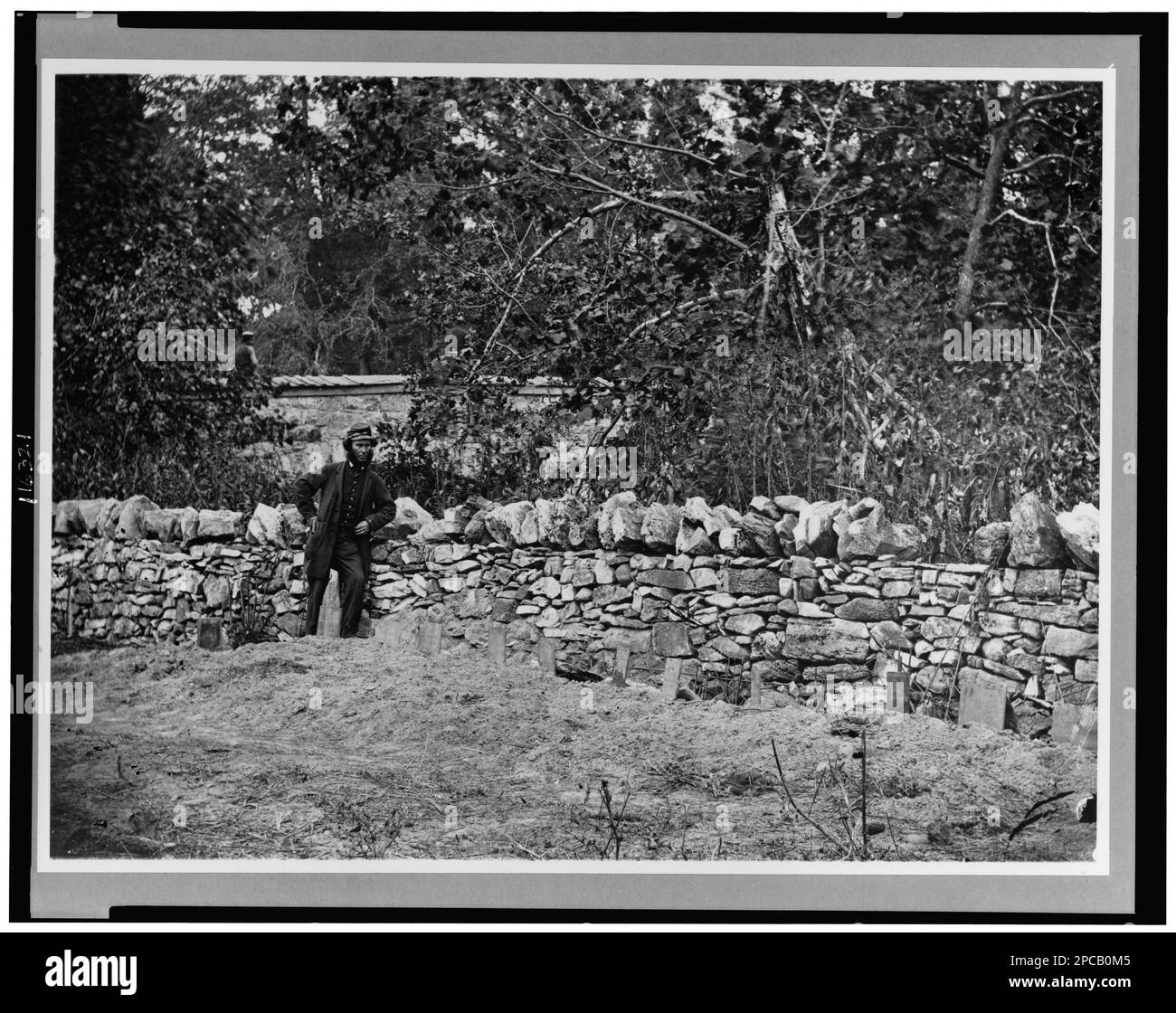 Soldier standing at graves of Federal soldiers, along stone fence, at Burnside Bridge, Antietam, Maryland. Civil War Photograph Collection , LC-B815-585. United States, History, Civil War, 1861-1865, Cemeteries, Union, United States, History, Civil War, 1861-1865, Military personnel, Union. Stock Photo
