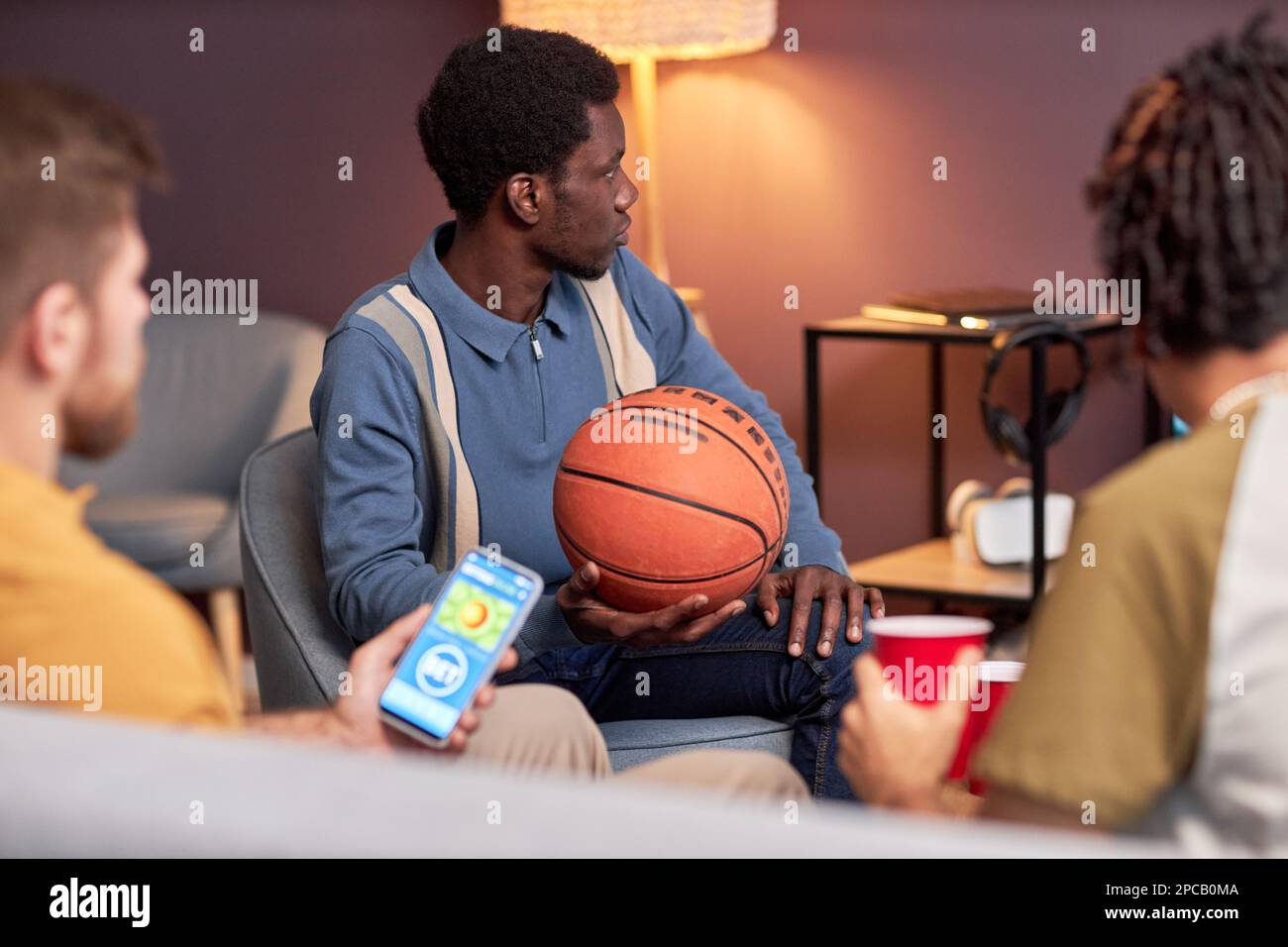 Side view at diverse group of sports fans watching basketball match at home and using online betting app Stock Photo