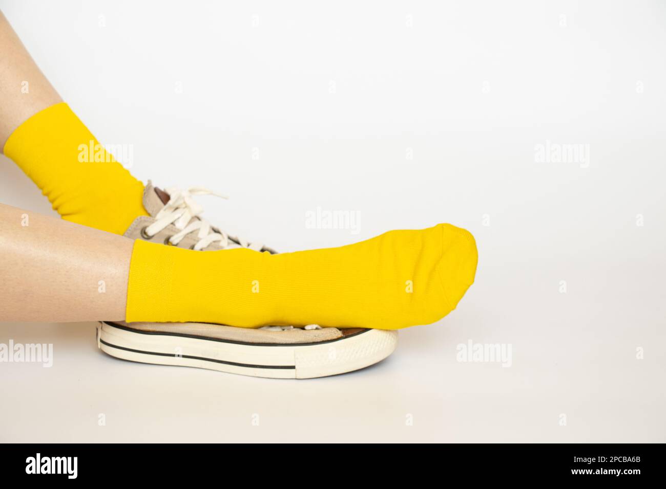 Women's legs in yellow socks and summer sports sneakers on a white background Stock Photo