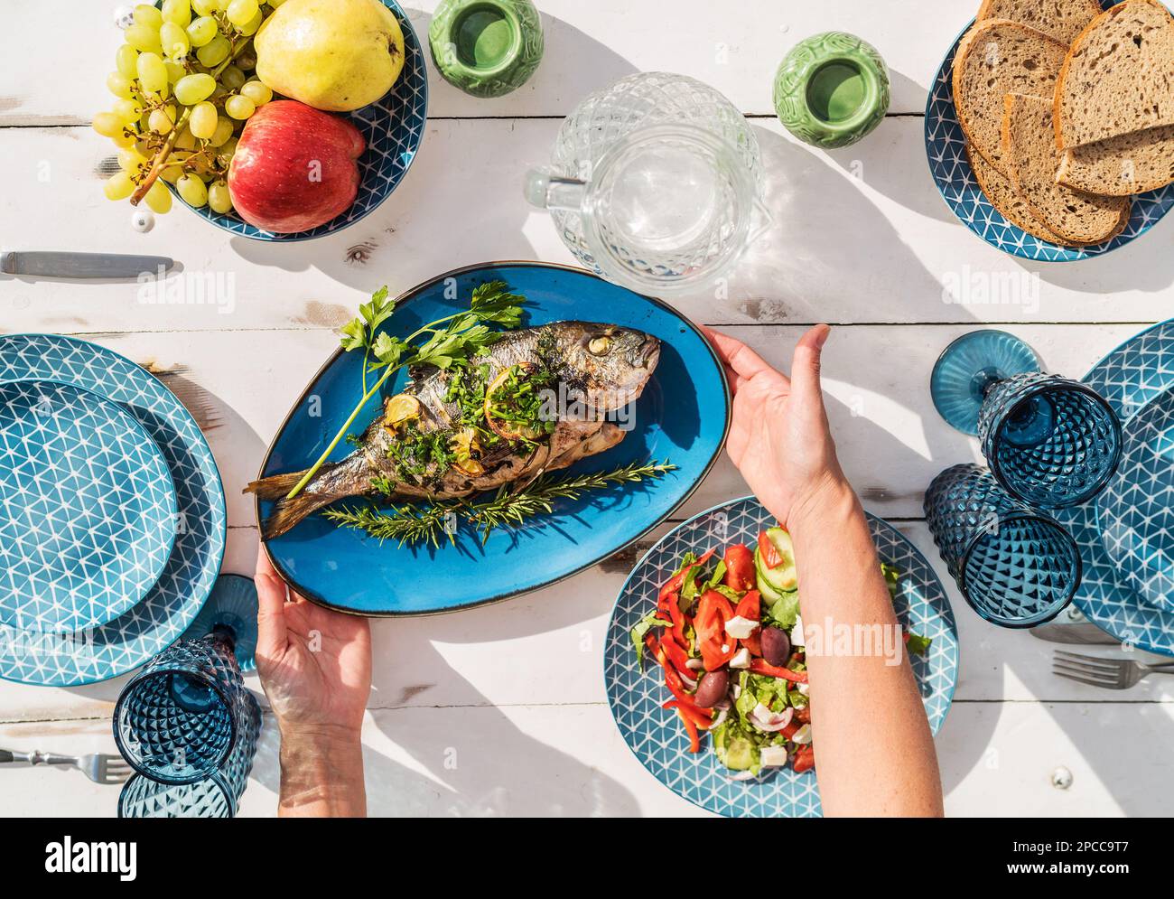 Gilt-head bream also known as Orata grilled on a barbeque grill served by a woman on a white wooden table with vegetable salad and fruits. Healthy sea Stock Photo