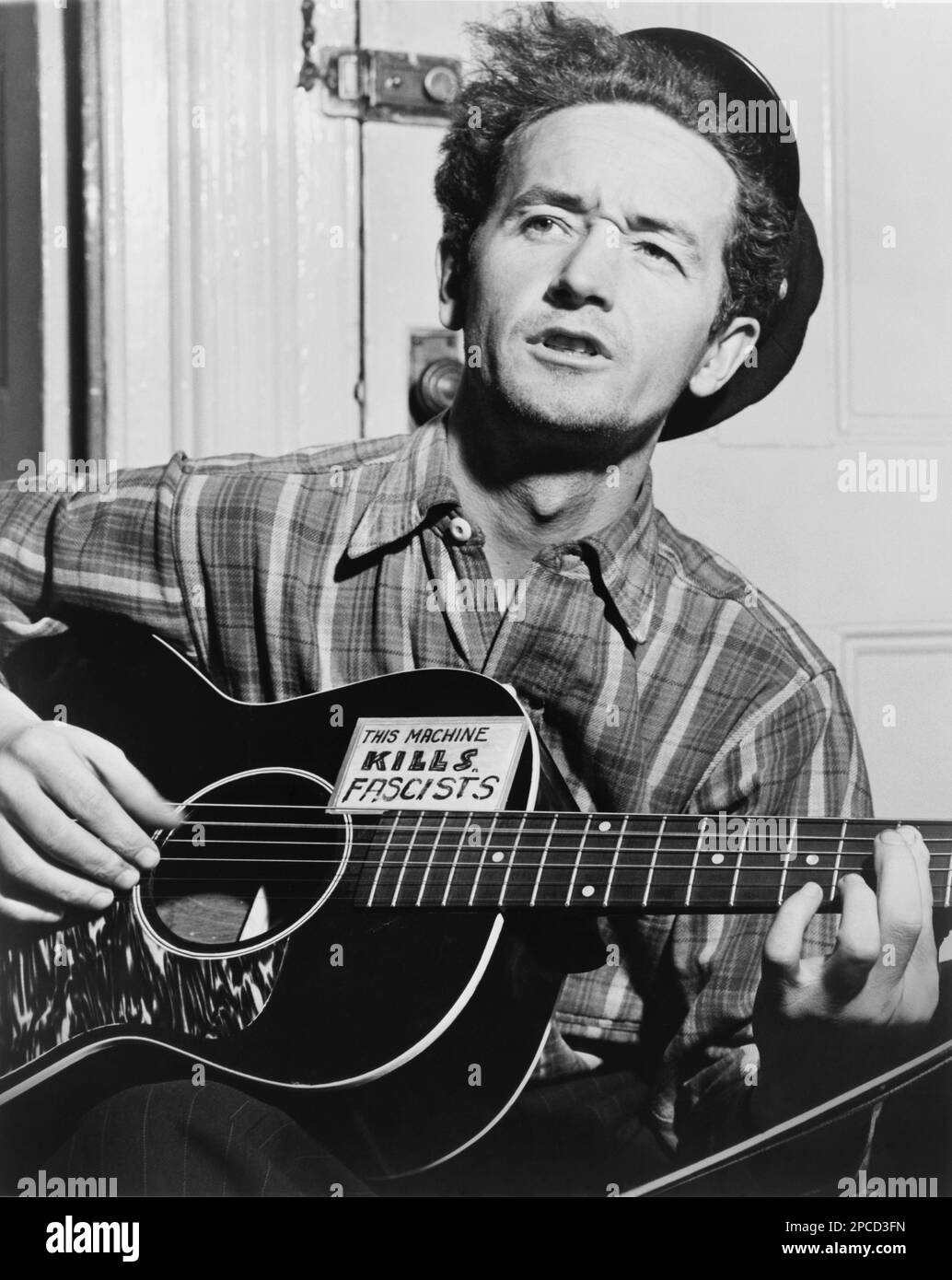 1943 , 8 march , USA :  The celebrated  american Country   singer  WOODY GUTHRIE (born Woodrow Wilson Guthrie , 1912 - 1967 ).  Photo by by Al Aumuller . Is best known as an American singer-songwriter and folk musician, whose musical legacy includes hundreds of political, traditional and children's songs, ballads and improvised works. He frequently performed with the slogan 'This Machine Kills Fascists' displayed on his guitar. His best known song is probably ' This Land Is Your Land '- CHITARRA - chitarrista - guitarist - MUSIC - ROCK - MUSICA LEGGERA - portrait - ritratto  - musicista - musi Stock Photo