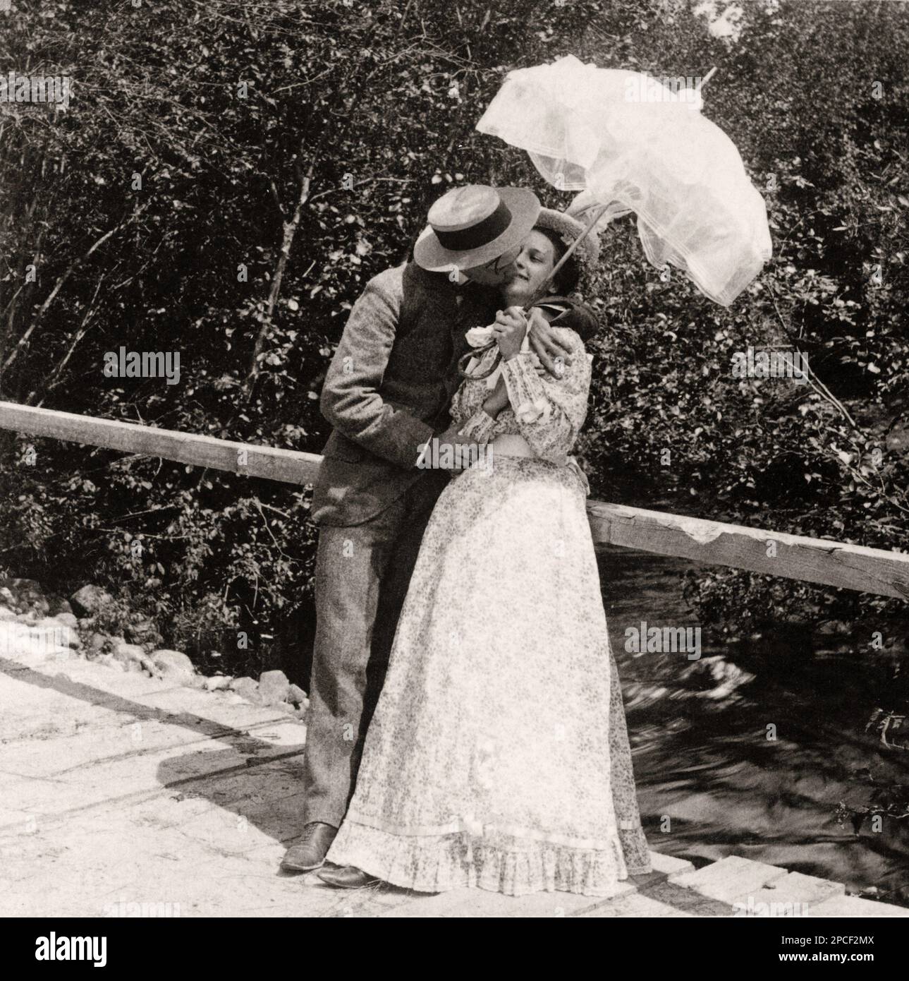 1897 , USA  : ' The Summer girl and her sweetheart ' . Man and woman kissing under umbrella on bridge . Photo by American Stereoscopic Co, New York    - KISS - BACIO -  KISSING - COURTSHIP - CORTEGGIAMENTO - LOVE - AMORE - LOVEERS - AMANTI - FIDANZATI - SAN VALENTINO - ST VALENTINE DAY - SENTIMENTAL - SENTIMENTALE - ROMANTIC - ROMANTICO -  FOTO STORICHE - HISTORY PHOTOS  -    - OTTOCENTO - 800's - '800 - FASHION - MODA - COPPIA - PORTRAIT - RITRATTO - pizzo - lace - BELLE EPOQUE  - ombrello - ombrellino da sole - pizzo - lace - hat - cappello - paglietta - ponte - ruscello -----  Archivio GBB Stock Photo