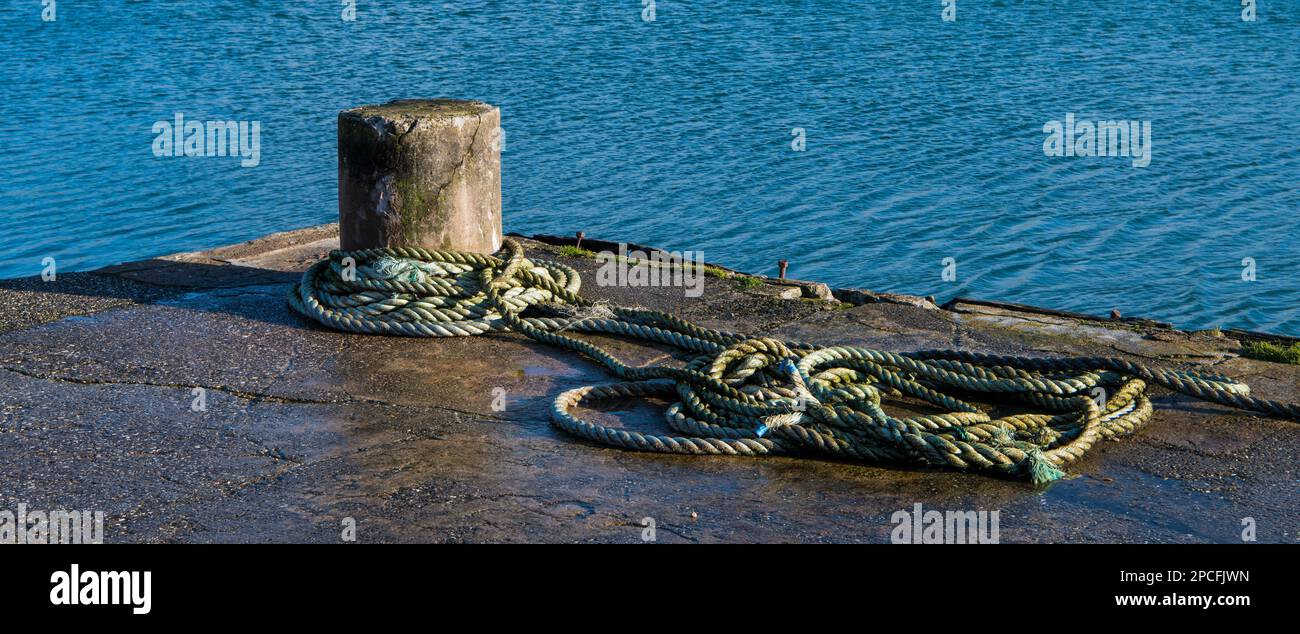 Nautical scene of a rustic concrete bollard and rope at a dock in