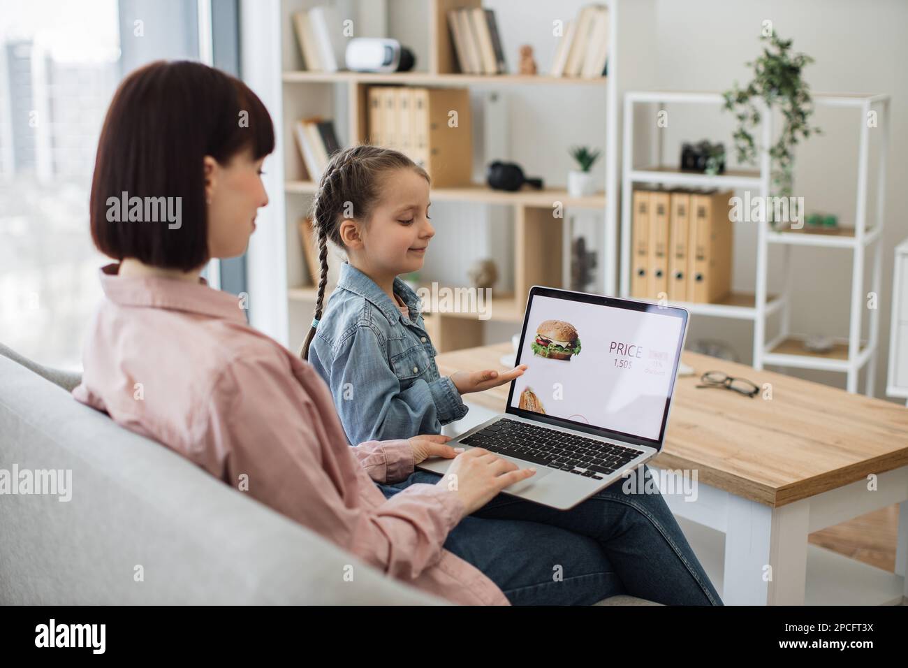 Attractive dark haired woman sitting on couch with her lovely daughter