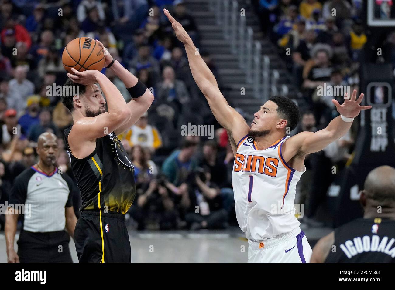 Golden State Warriors guard Klay Thompson, left, makes a 3-point basket  against Phoenix Suns guard Devin Booker (1) during the first half of an NBA  basketball game in San Francisco, Monday, March