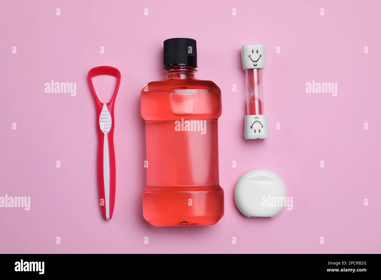 Tongue cleaner, dental floss, mouthwash and hourglass on pink