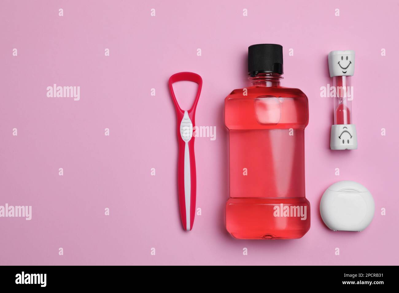 Tongue cleaner, dental floss, mouthwash and hourglass on pink