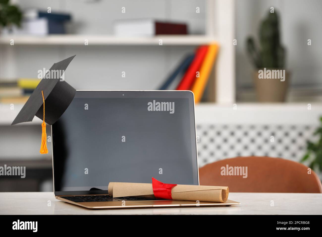 Graduation hat, student's diploma and laptop on white table indoors ...