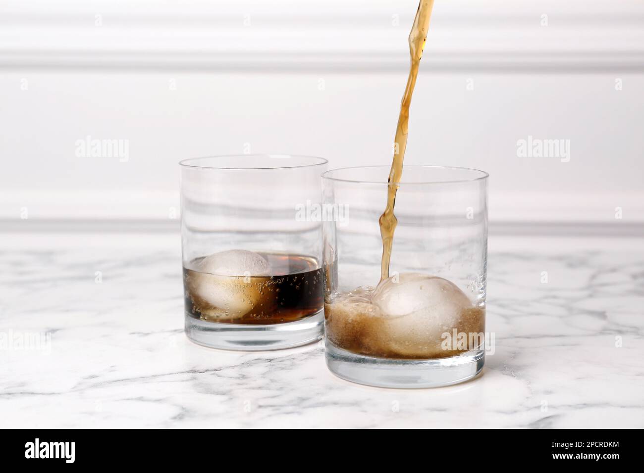 https://c8.alamy.com/comp/2PCRDKM/pouring-cocktail-into-glass-with-ice-ball-on-white-marble-table-2PCRDKM.jpg