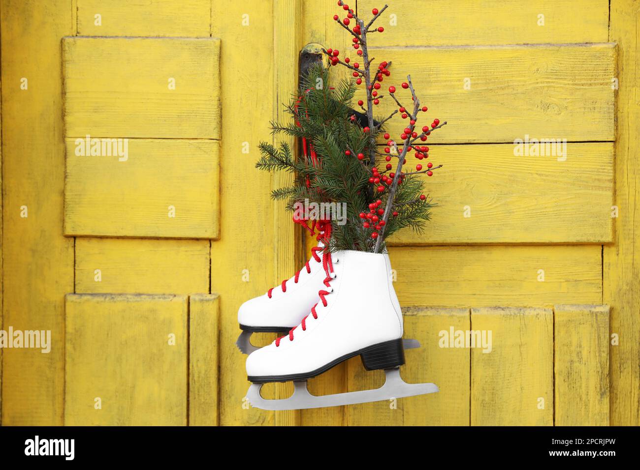 Pair of ice skates with Christmas decor hanging on old yellow door