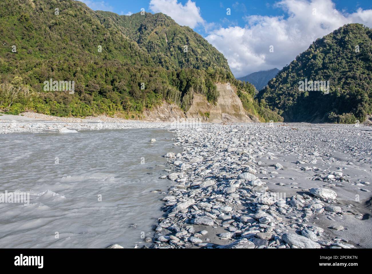 The Waiho river full of glacial melt water flows out of the hilly landscape in the South island of Aotearoa New Zealand. Stock Photo