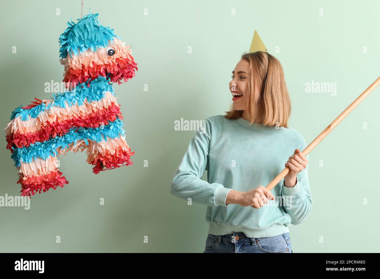 Young woman breaking Mexican pinata on green background Stock Photo - Alamy