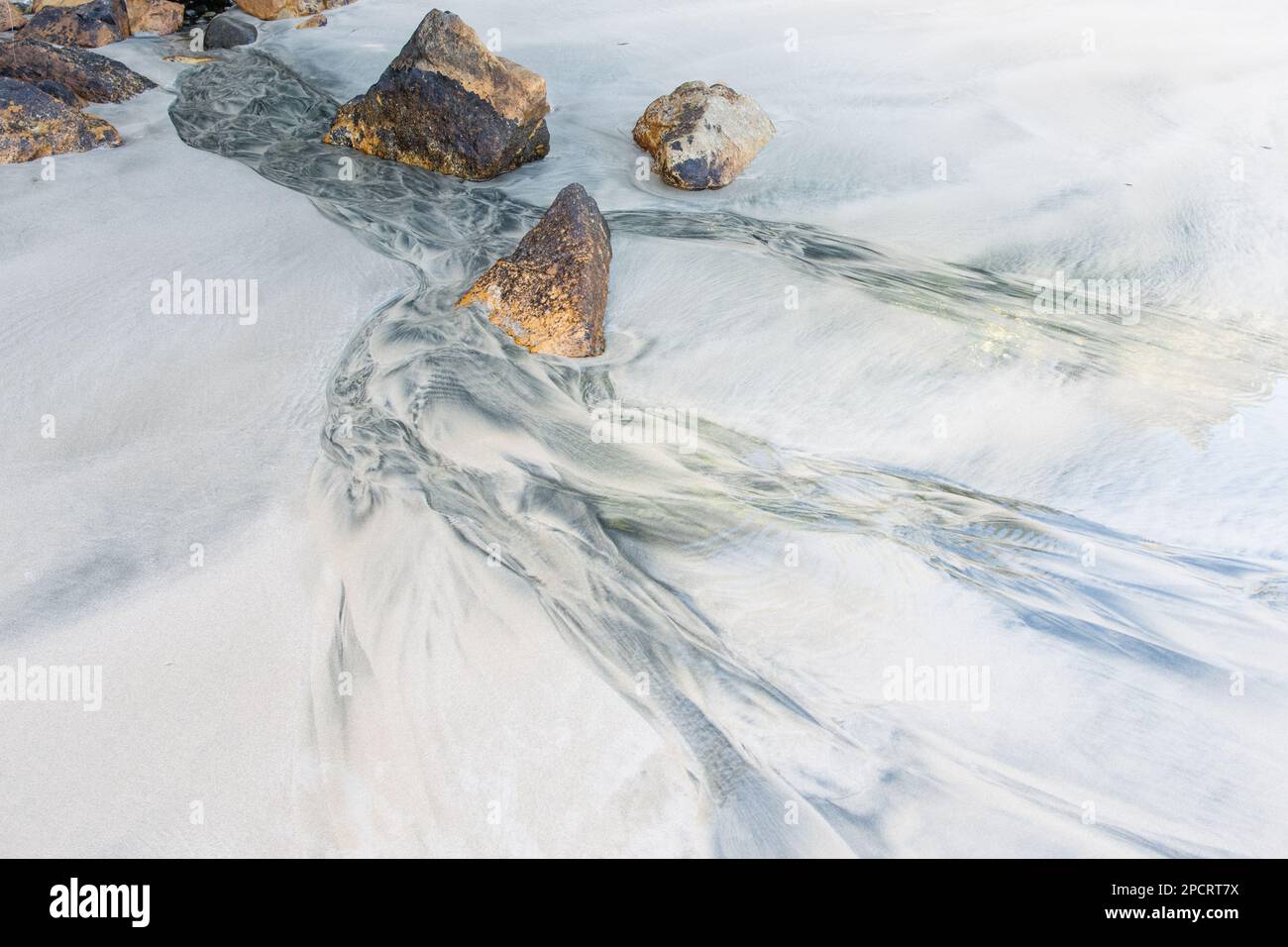 Natural patterns formed on the white sand beach in Stewart Island, New Zealand as freshwater flows onto the beach and forms an alluvial fan. Stock Photo