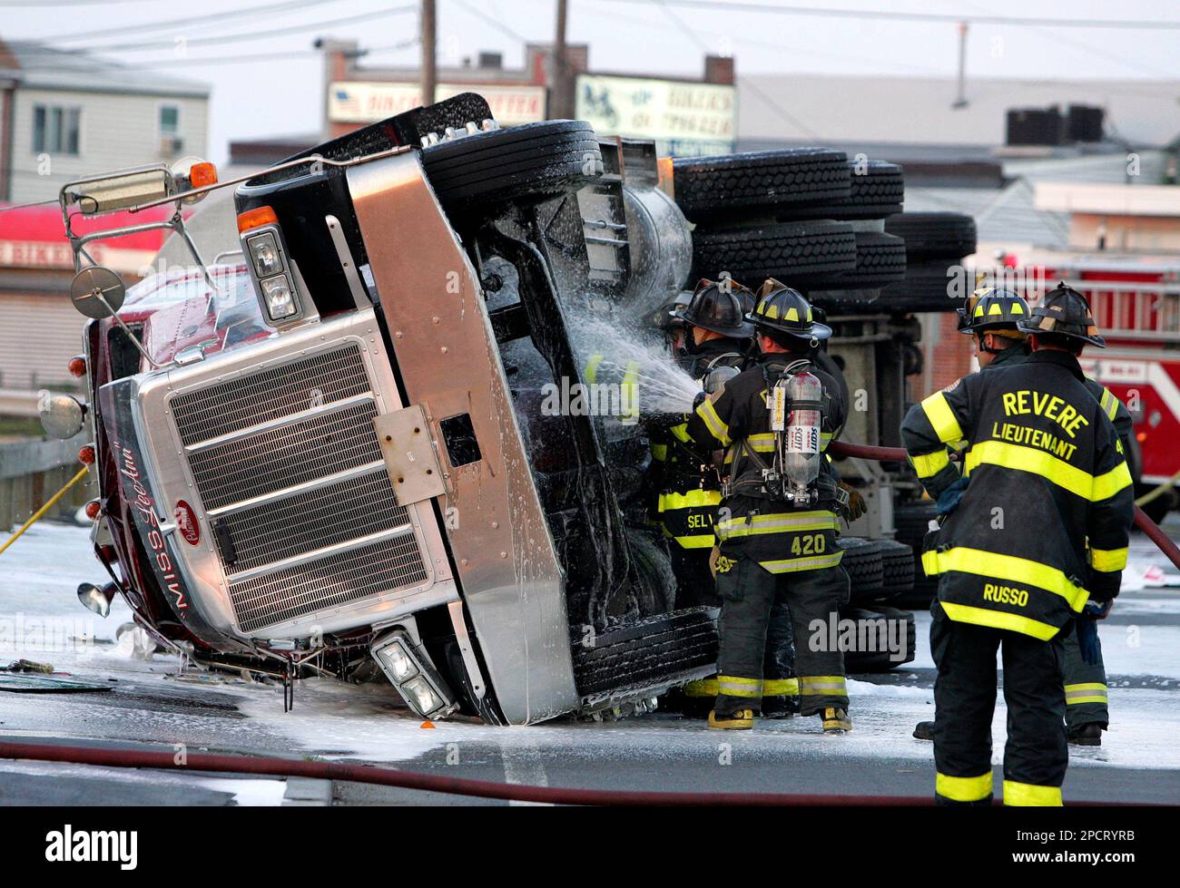 Firefighters spray foam on a gasoline tanker truck that overturned in a ...