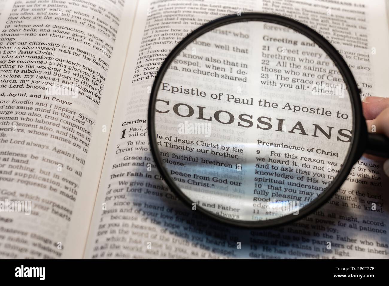 A closeup of a person holding a magnifier and reading the book of Colossians from the New Testament Stock Photo